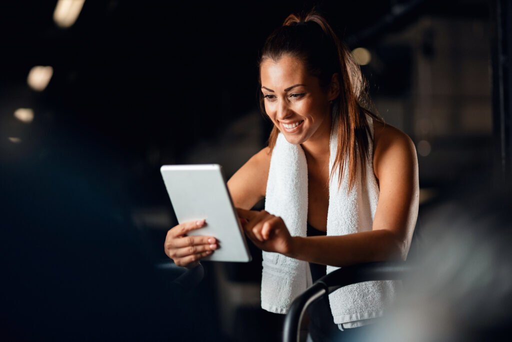 App deportiva IA una chica en le gym sonriente mientra mira su tableta